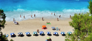 beach with people under blue and white umbrellas and playing in the ocean